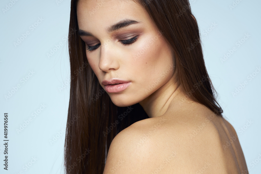 Pretty brunette with bared shoulders long hair body care blue background Pretty brunette with bared shoulders long hair body care blue background