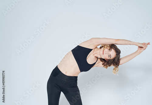 A woman in leggings has joined her hands above her head and is doing the exercises, bends to the side