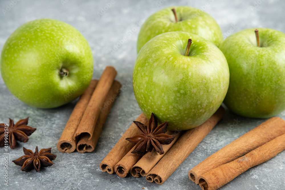 Four green apple and cinnamon sticks on marble background