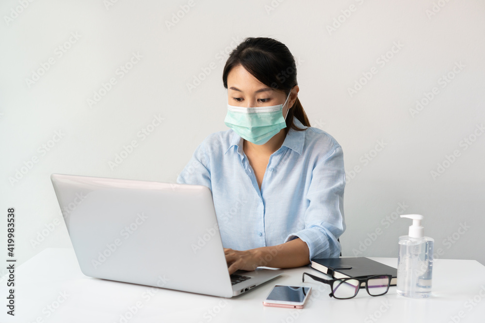 Asian businesswoman working at workplace and wearing a face mask during the coronavirus crisis. Working from home, business and health care concept. Asian businesswoman working at workplace and wearing a face mask during the coronavirus crisis. Working from home, business and health care concept.
