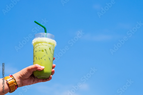 Woman's hand showing a cup of cold green tea with sky background in bright sunny day.
