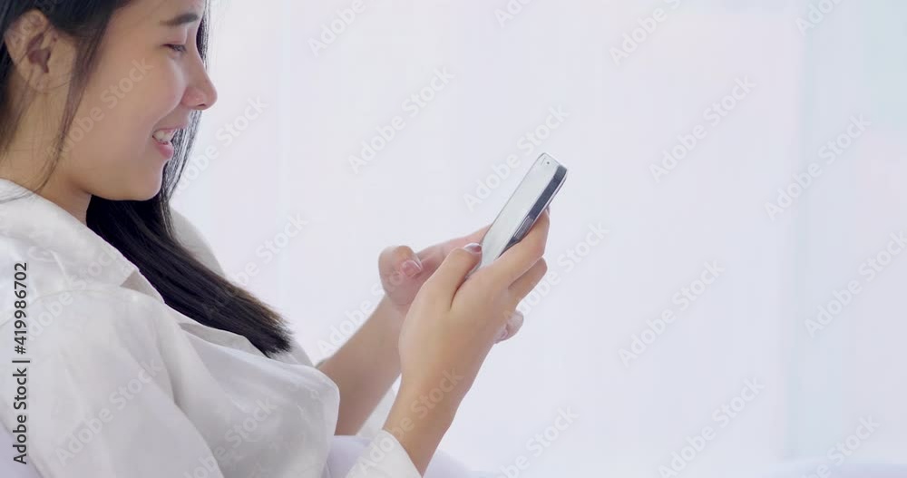 Young blogger Asian woman using smartphone social media to check rating response online page and writing to communicate with fan to keep relation. Relaxing chatting to friend on the bed in white shirt Young blogger Asian woman using smartphone social media to check rating response online page and writing to communicate with fan to keep relation. Relaxing chatting to friend on the bed in white shirt