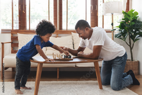 African American Father and son playing chess in living room together. Happy Black Family engaged in board game on holiday.