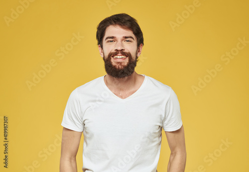A man in a white T-shirt gestures with his hands on a yellow background Copy Space
