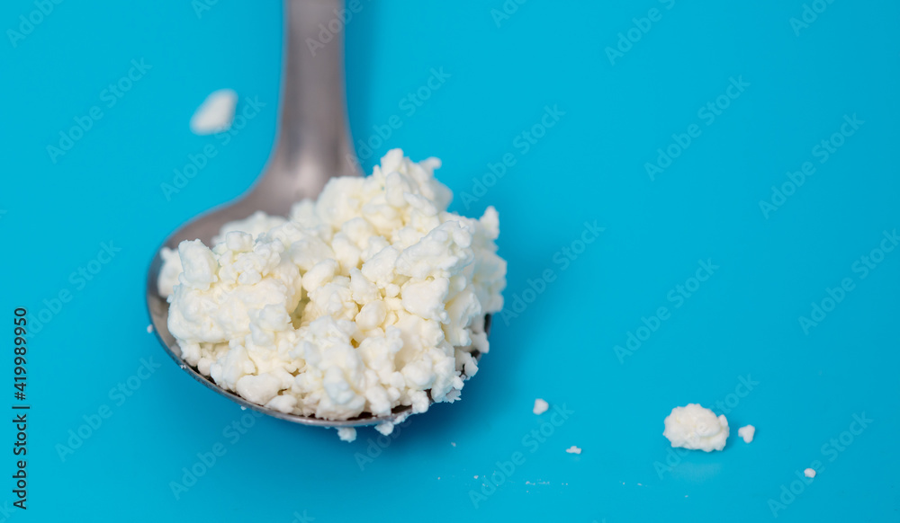 Milk curd in a spoon on a blue background. Milk curd in a spoon on a blue background.