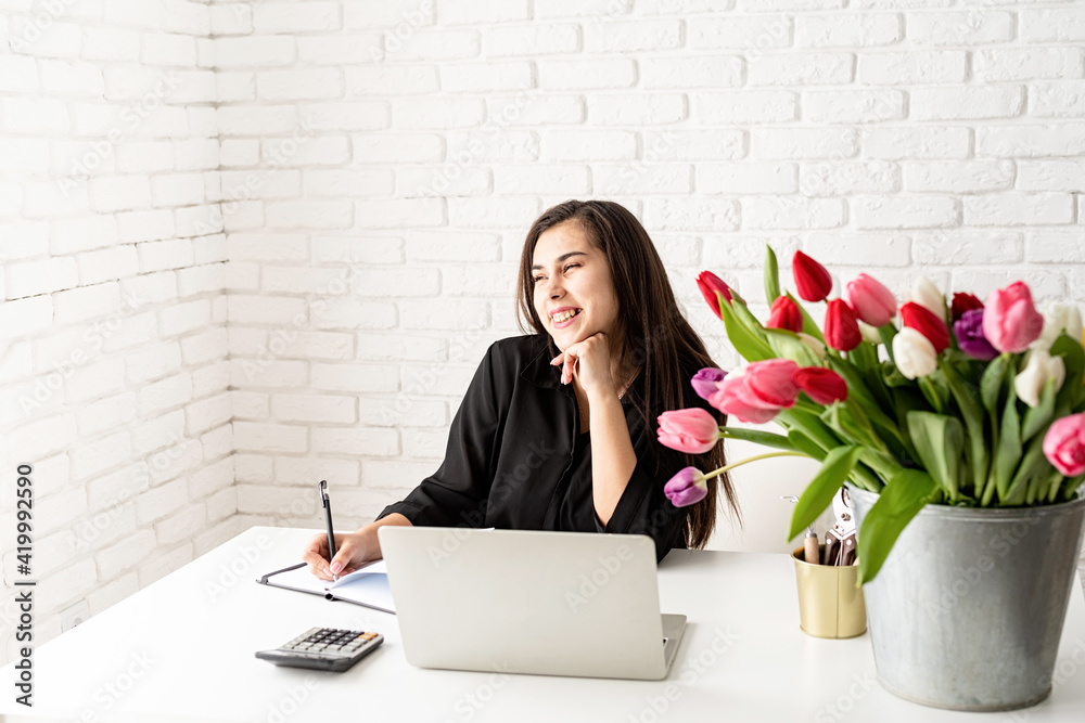young laughing business woman florist writing in notebook, using laptop in the office young laughing business woman florist writing in notebook, using laptop in the office
