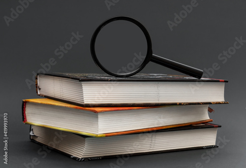 Magnifying glass on stack of books on black background.