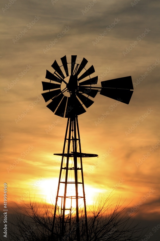 Kansas Windmill silhouette with a tree and colorful sky with clouds north of Hutchinson Kansas USA out in the country.