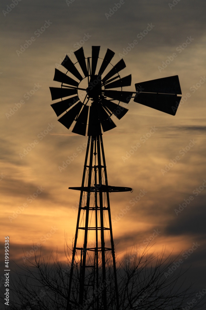 Kansas Windmill silhouette with a tree and colorful sky with clouds north of Hutchinson Kansas USA out in the country.
