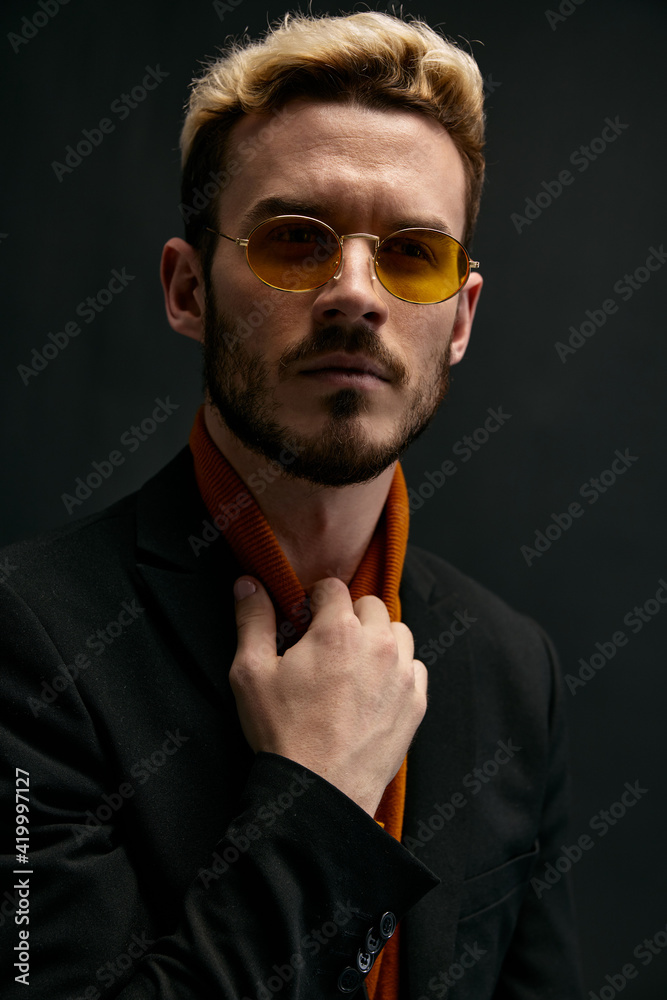 Obraz premium stylish man with glasses blond black jacket orange sweater dark background