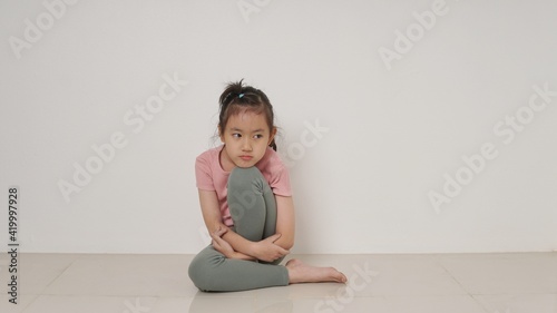 Sad little girl sitting against the wall in despair