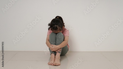 Sad little girl sitting against the wall in despair