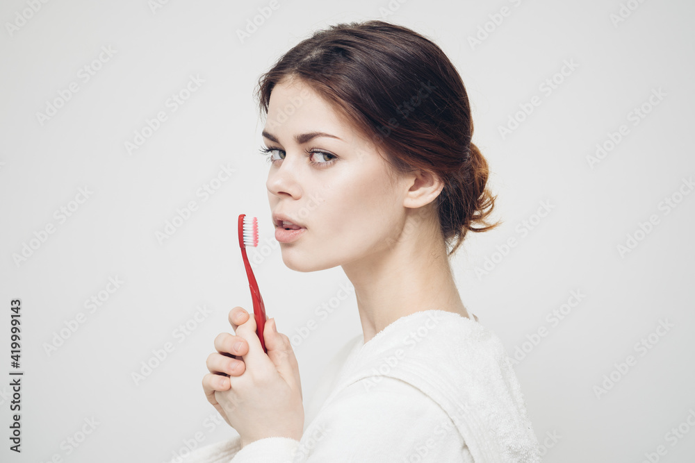 emotional woman with a toothbrush in her hand on a light background and a white robe side view
