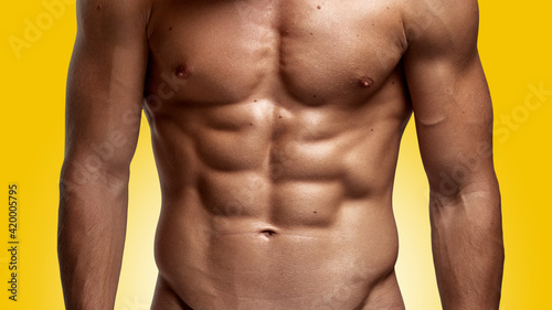 Closeup image of a strong athletic man showing muscular body and sixpack abs over yellow background.