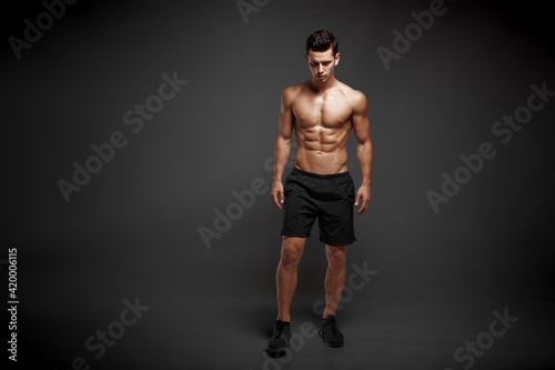 Full length image of a strong athletic man showing muscular body and sixpack abs isolated black background.