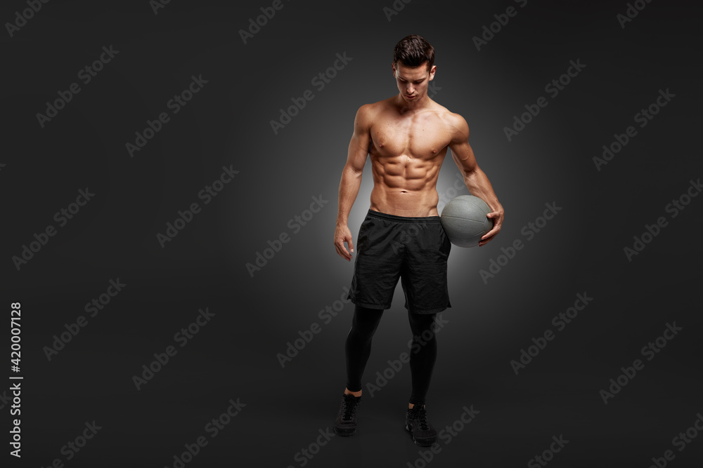 Full length of a handsome brunette young man with muscular body holding a bascket ball, isolated black background.