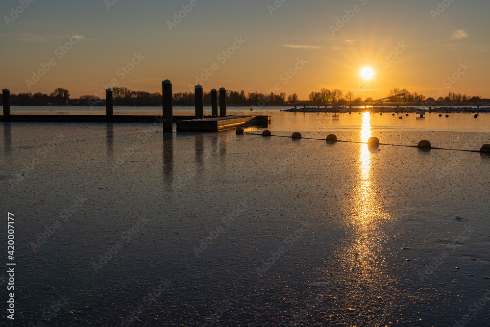 A colorful sunset at a frozen lake Zoetermeerse Plas with buoys and boat dock in Zoetermeer