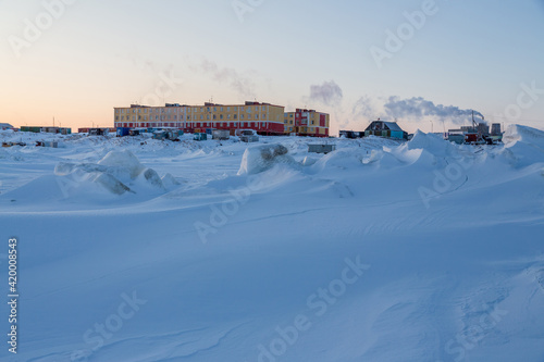 Winter arctic landscape. View of a small arctic village on the shores of the frozen sea. Multi-colored residential buildings. Cold weather. Harsh polar climate. Tavayvaam, Chukotka, Siberia, Russia.