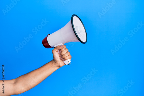 Hand of hispanic man holding megaphone over isolated blue background.