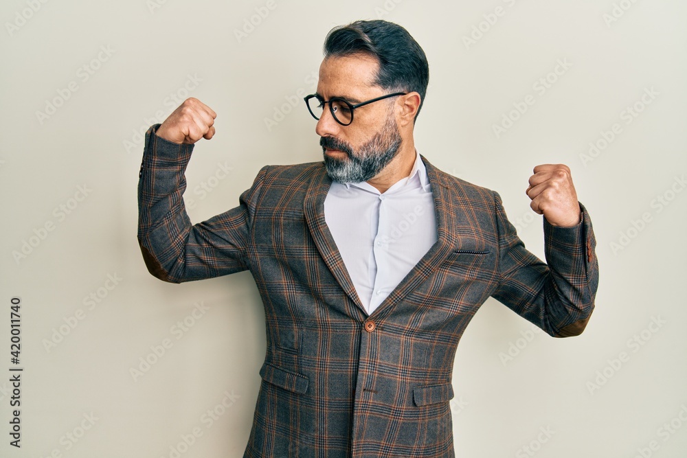 Middle age man with beard and grey hair wearing business jacket and glasses showing arms muscles smiling proud. fitness concept. Middle age man with beard and grey hair wearing business jacket and glasses showing arms muscles smiling proud. fitness concept.