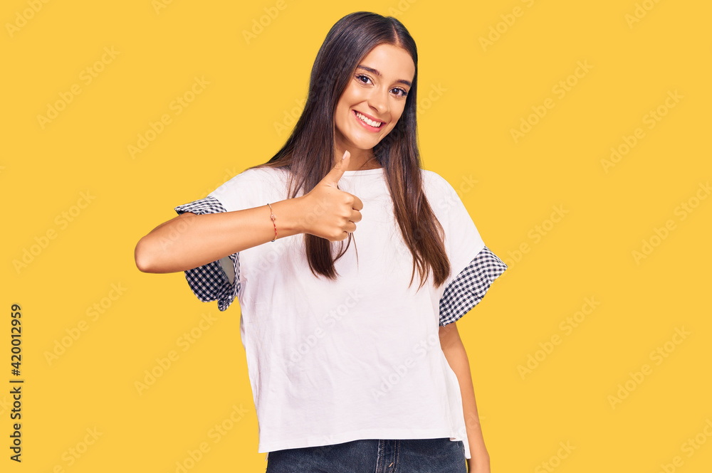 Young hispanic woman wearing casual clothes doing happy thumbs up gesture with hand. approving expression looking at the camera showing success. Young hispanic woman wearing casual clothes doing happy thumbs up gesture with hand. approving expression looking at the camera showing success.