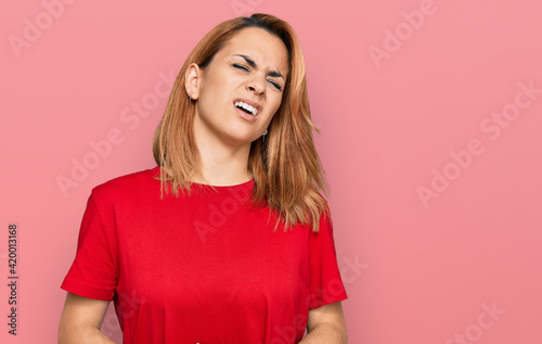 Hispanic young woman wearing casual red t shirt with hand on stomach because nausea, painful disease feeling unwell. ache concept. © Krakenimages.com