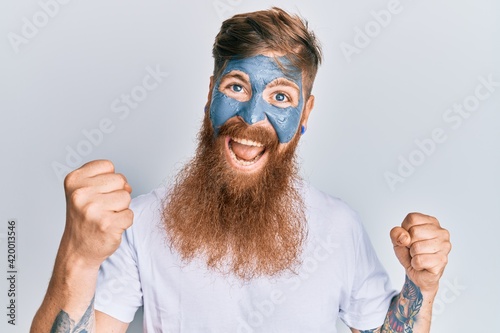 Young irish redhead man wearing facial mask screaming proud, celebrating victory and success very excited with raised arms