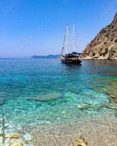 Blue and turquoise crystal clear waters of a rocky beach in south Turkey with a tourist leisure boat in the background