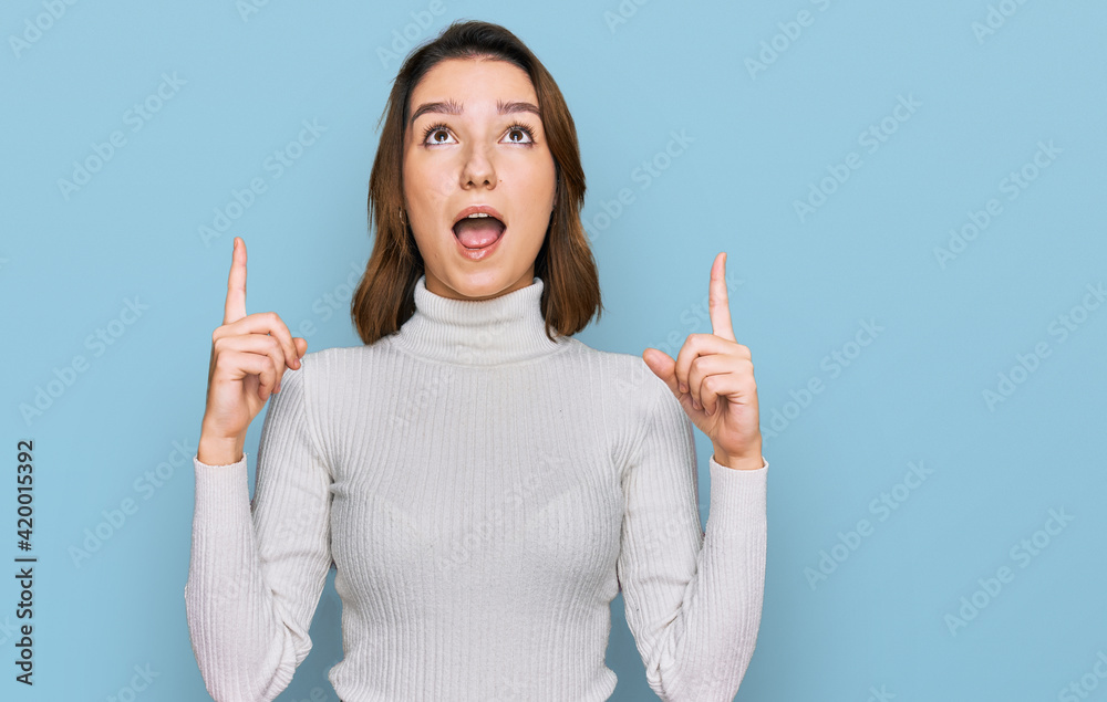 Young caucasian girl wearing casual clothes amazed and surprised looking up and pointing with fingers and raised arms. Young caucasian girl wearing casual clothes amazed and surprised looking up and pointing with fingers and raised arms.