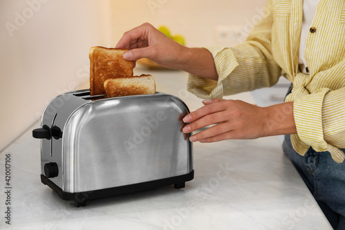 Woman taking slice of bread from toaster in kitchen, closeup