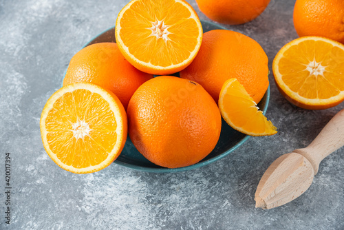 Fototapeta Naklejka Na Ścianę i Meble -  A bowl full of sliced and whole juicy orange fruits with wooden reamer
