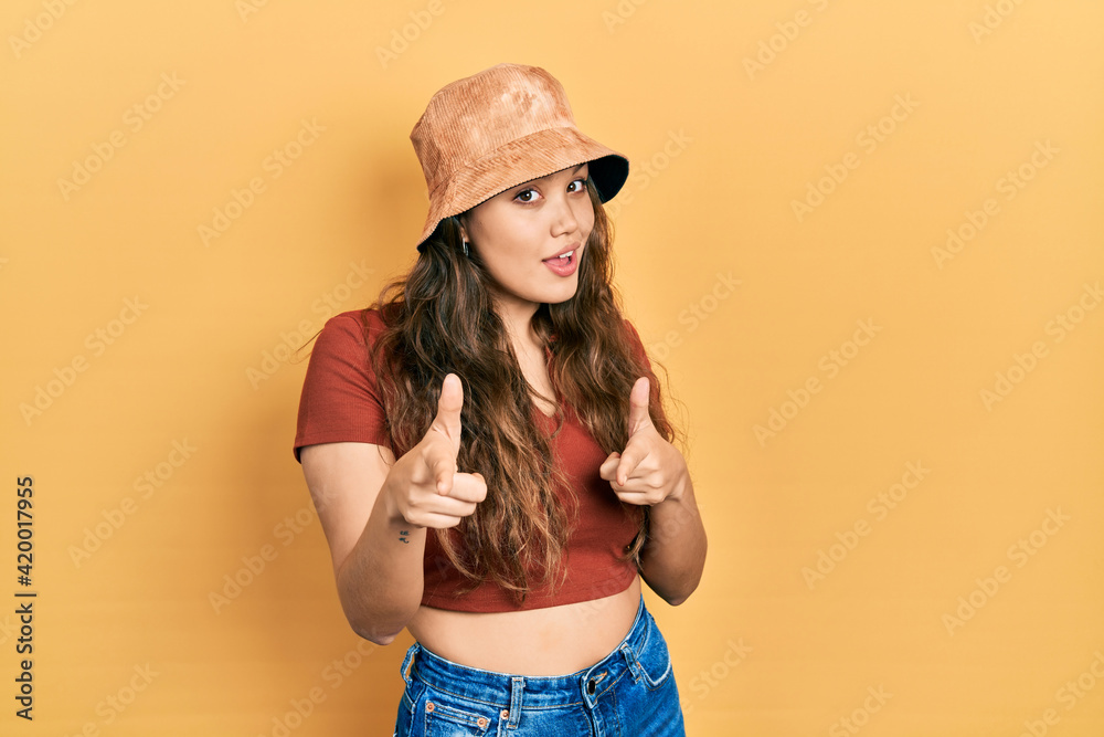 Young hispanic girl wearing casual clothes and hat pointing fingers to camera with happy and funny face. good energy and vibes. Young hispanic girl wearing casual clothes and hat pointing fingers to camera with happy and funny face. good energy and vibes.