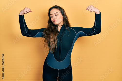 Εκτύπωση καμβά Young hispanic girl wearing diver neoprene uniform showing arms muscles smiling proud