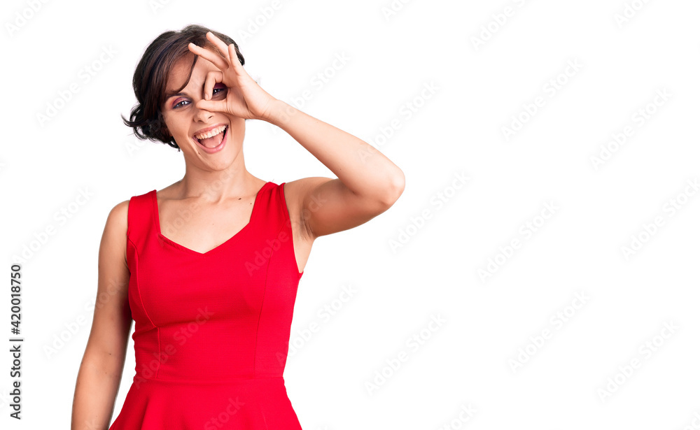 Beautiful young woman with short hair wearing casual style with sleeveless shirt doing ok gesture with hand smiling, eye looking through fingers with happy face. Beautiful young woman with short hair wearing casual style with sleeveless shirt doing ok gesture with hand smiling, eye looking through fingers with happy face.