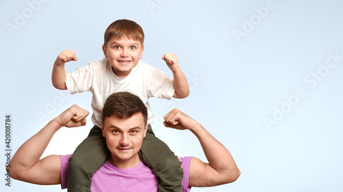 child sits on dad's shoulders on blue background. father and child show strength with space for text. Happy father's day.  