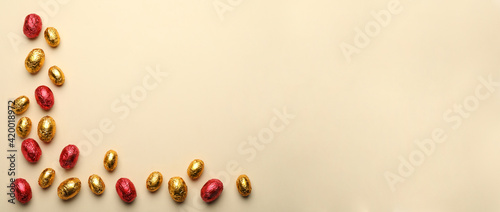 Chocolate eggs wrapped in red and golden foil on beige background, flat lay. Space for text