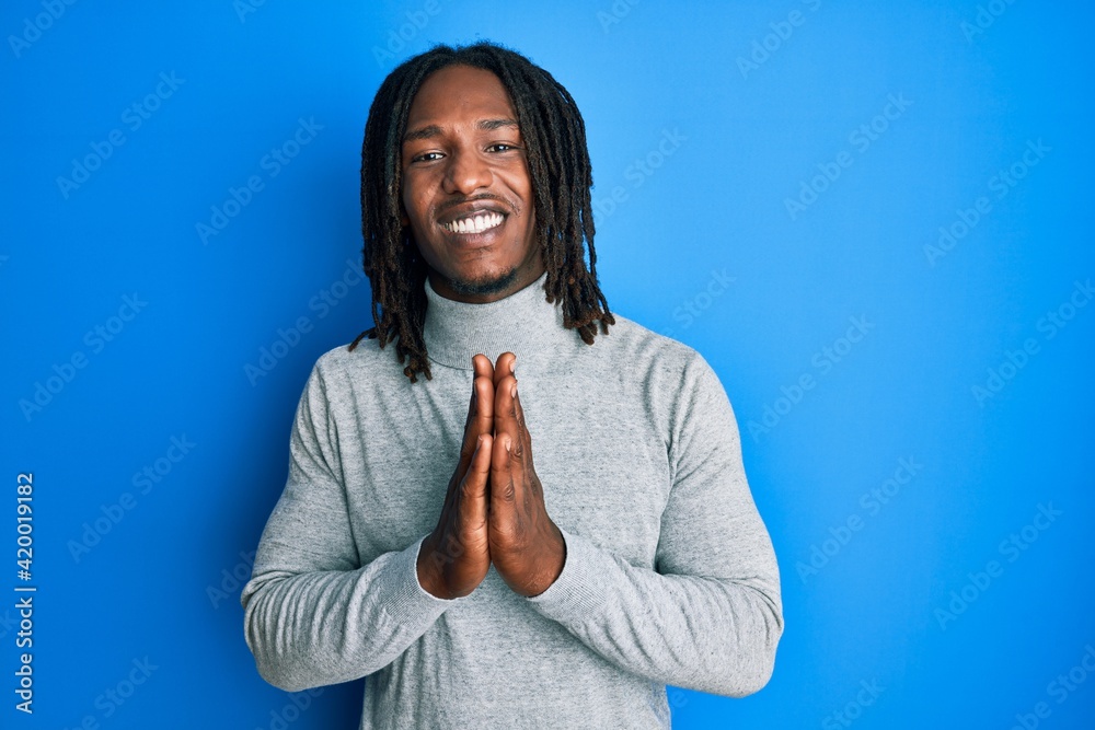 African american man with braids wearing turtleneck sweater praying with hands together asking for forgiveness smiling confident. African american man with braids wearing turtleneck sweater praying with hands together asking for forgiveness smiling confident.