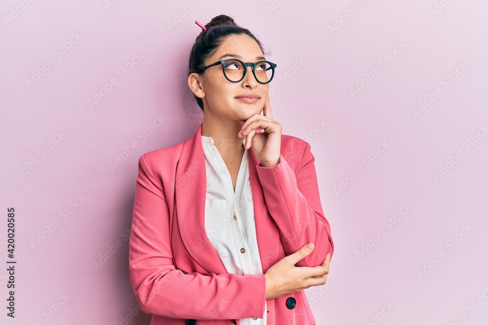 Beautiful middle eastern woman wearing business jacket and glasses with hand on chin thinking about question, pensive expression. smiling and thoughtful face. doubt concept. Beautiful middle eastern woman wearing business jacket and glasses with hand on chin thinking about question, pensive expression. smiling and thoughtful face. doubt concept.
