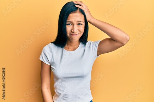 Beautiful hispanic woman wearing casual white tshirt confuse and wonder about question. uncertain with doubt, thinking with hand on head. pensive concept.