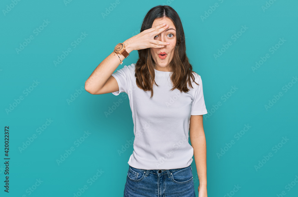 Young beautiful woman wearing casual white t shirt peeking in shock covering face and eyes with hand, looking through fingers with embarrassed expression. Young beautiful woman wearing casual white t shirt peeking in shock covering face and eyes with hand, looking through fingers with embarrassed expression.