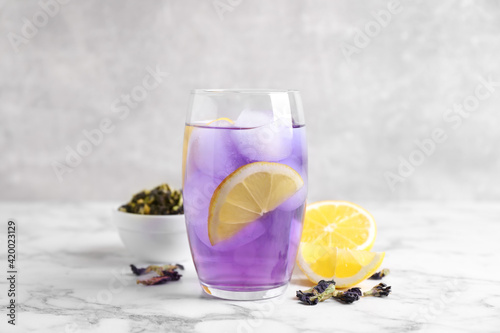 Glass of organic blue Anchan with lemon and ice on white marble table. Herbal tea
