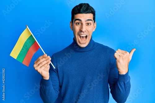 Handsome hispanic man holding lithuania flag pointing thumb up to the side smiling happy with open mouth photo