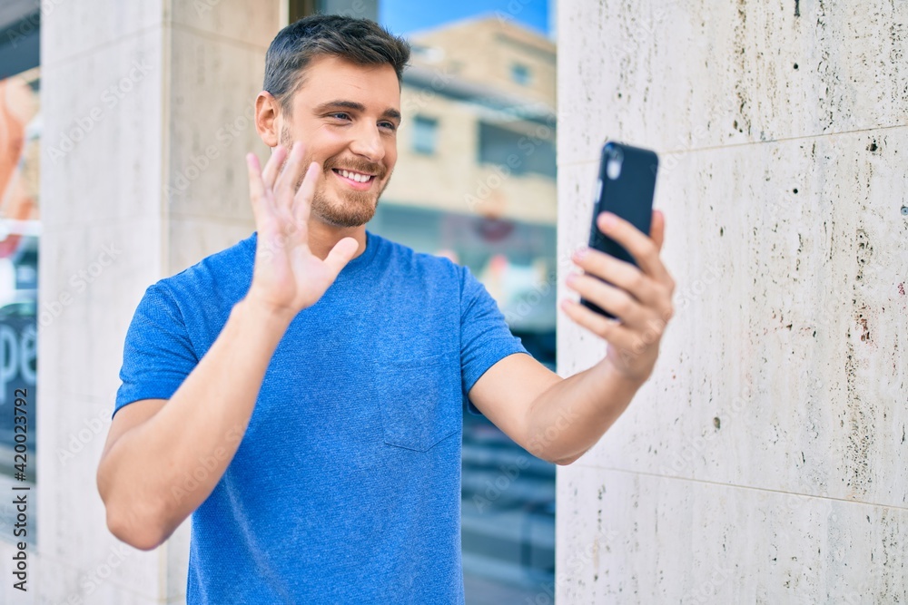 Young caucasian man smiling happy doing video call using smartphone at the city. Young caucasian man smiling happy doing video call using smartphone at the city.