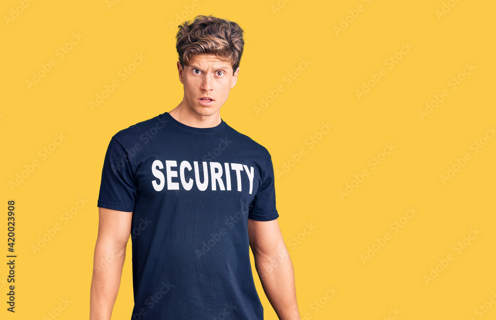 Young handsome man wearing security t shirt in shock face, looking skeptical and sarcastic, surprised with open mouth Young handsome man wearing security t shirt in shock face, looking skeptical and sarcastic, surprised with open mouth