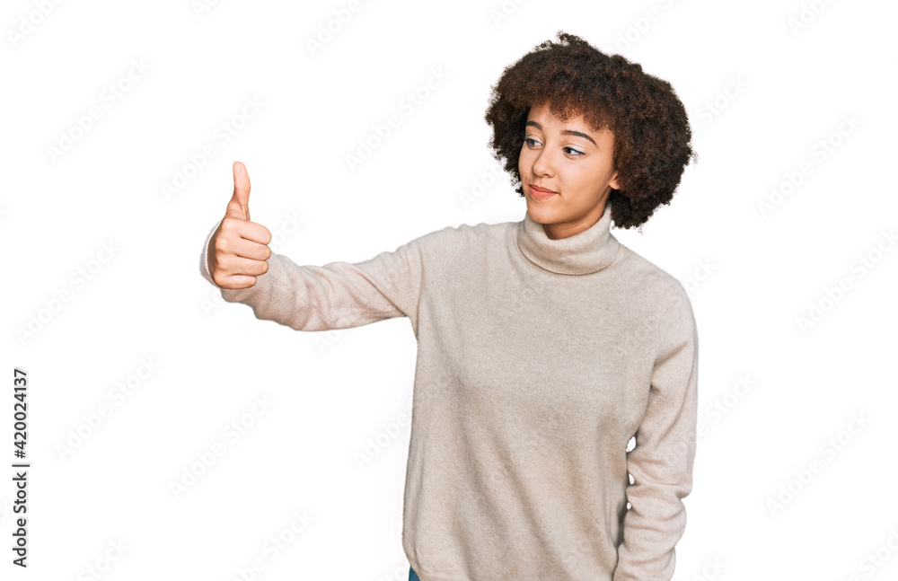 Young hispanic girl wearing wool winter sweater looking proud, smiling doing thumbs up gesture to the side Young hispanic girl wearing wool winter sweater looking proud, smiling doing thumbs up gesture to the side