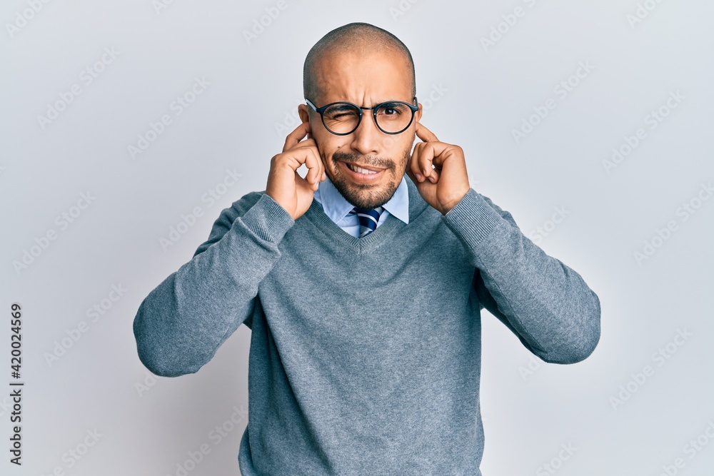 Hispanic adult man wearing glasses and business style covering ears with fingers with annoyed expression for the noise of loud music. deaf concept. Hispanic adult man wearing glasses and business style covering ears with fingers with annoyed expression for the noise of loud music. deaf concept.