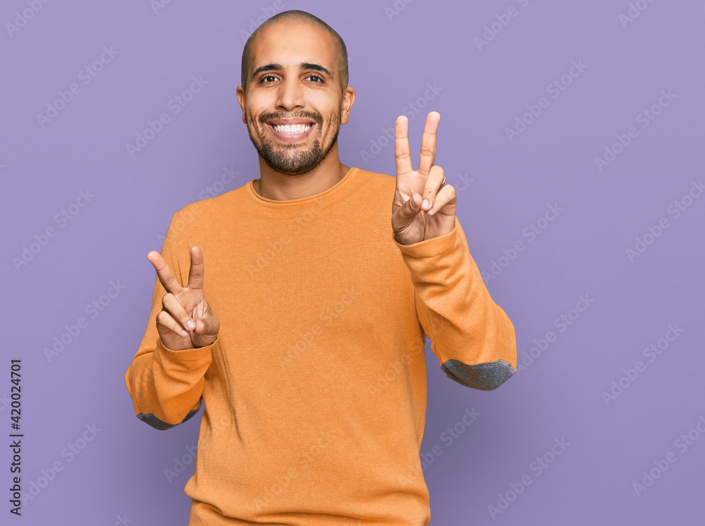 Hispanic adult man wearing casual winter sweater smiling looking to the camera showing fingers doing victory sign. number two. Hispanic adult man wearing casual winter sweater smiling looking to the camera showing fingers doing victory sign. number two.