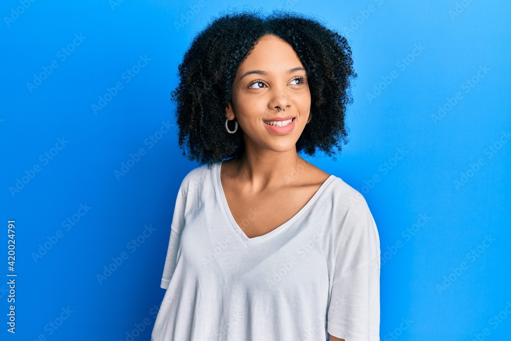 Young african american girl wearing casual white t shirt looking to side, relax profile pose with natural face and confident smile. Young african american girl wearing casual white t shirt looking to side, relax profile pose with natural face and confident smile.