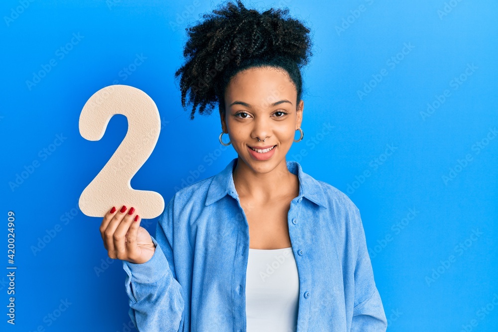 Young african american girl holding number two looking positive and happy standing and smiling with a confident smile showing teeth Young african american girl holding number two looking positive and happy standing and smiling with a confident smile showing teeth