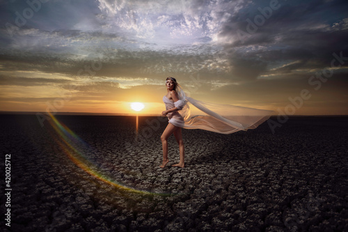Beautiful blonde woman is posing in maxi yellow dress on desert with naked sexy legs. Summer photo. Fashion model  glamorous girl posing in the desert. Long hair flying in wind.